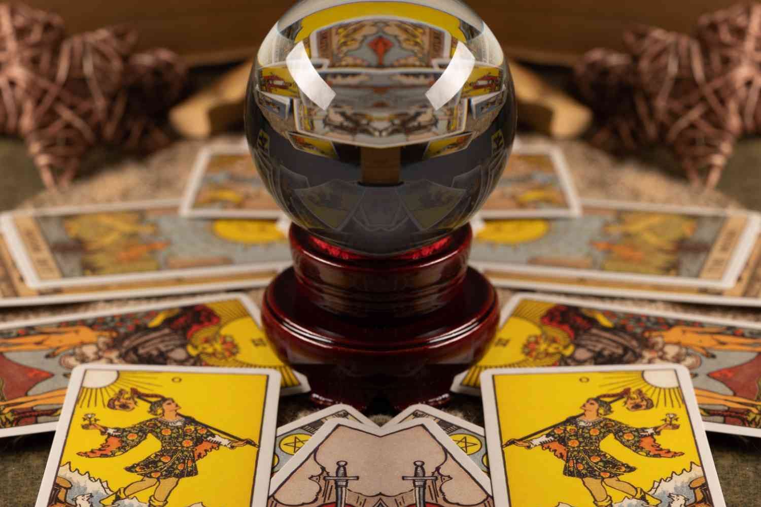 En kristallkula på ett bord omgiven av tarotkort med mystiska motiv.